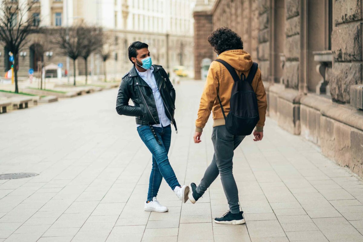 Two people walking down a sidewalk wearing masks.